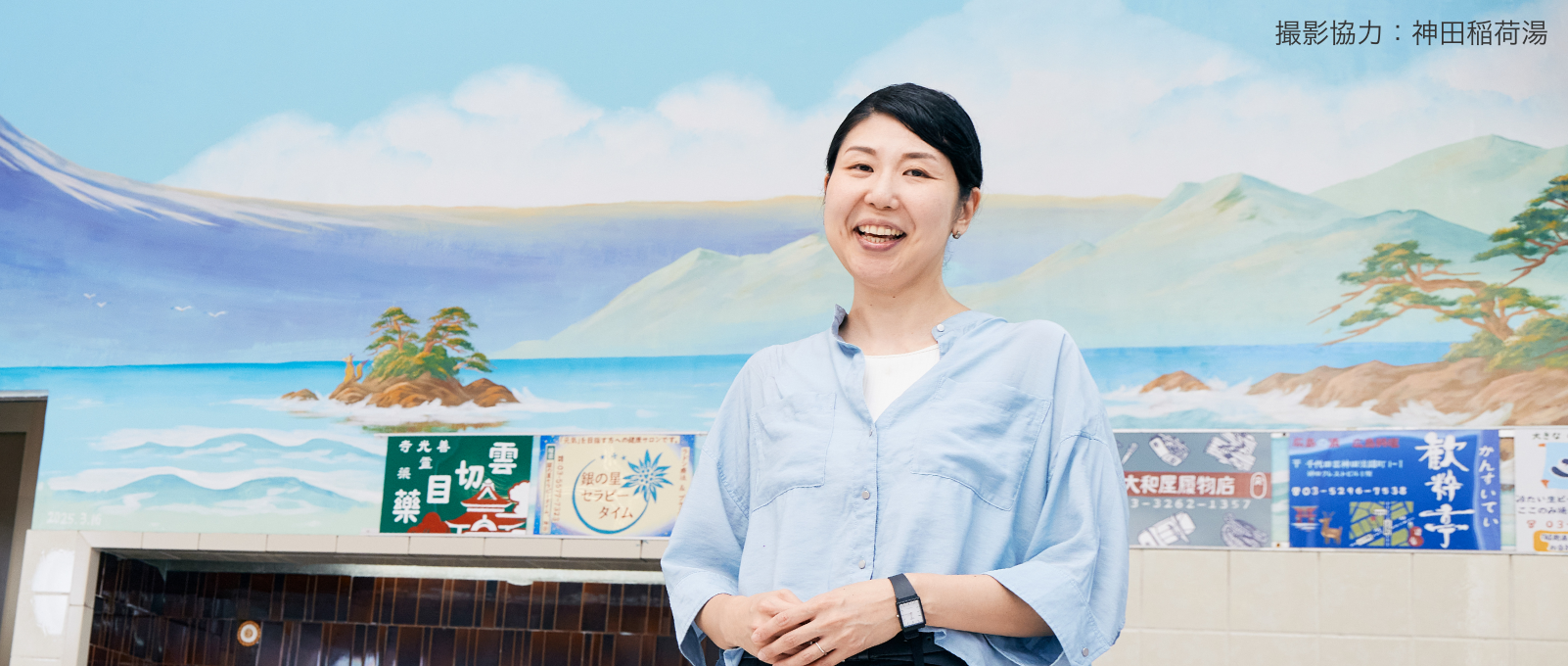 撮影協力：神田稲荷湯 銭湯のペンキ絵の前に立つ田中さん